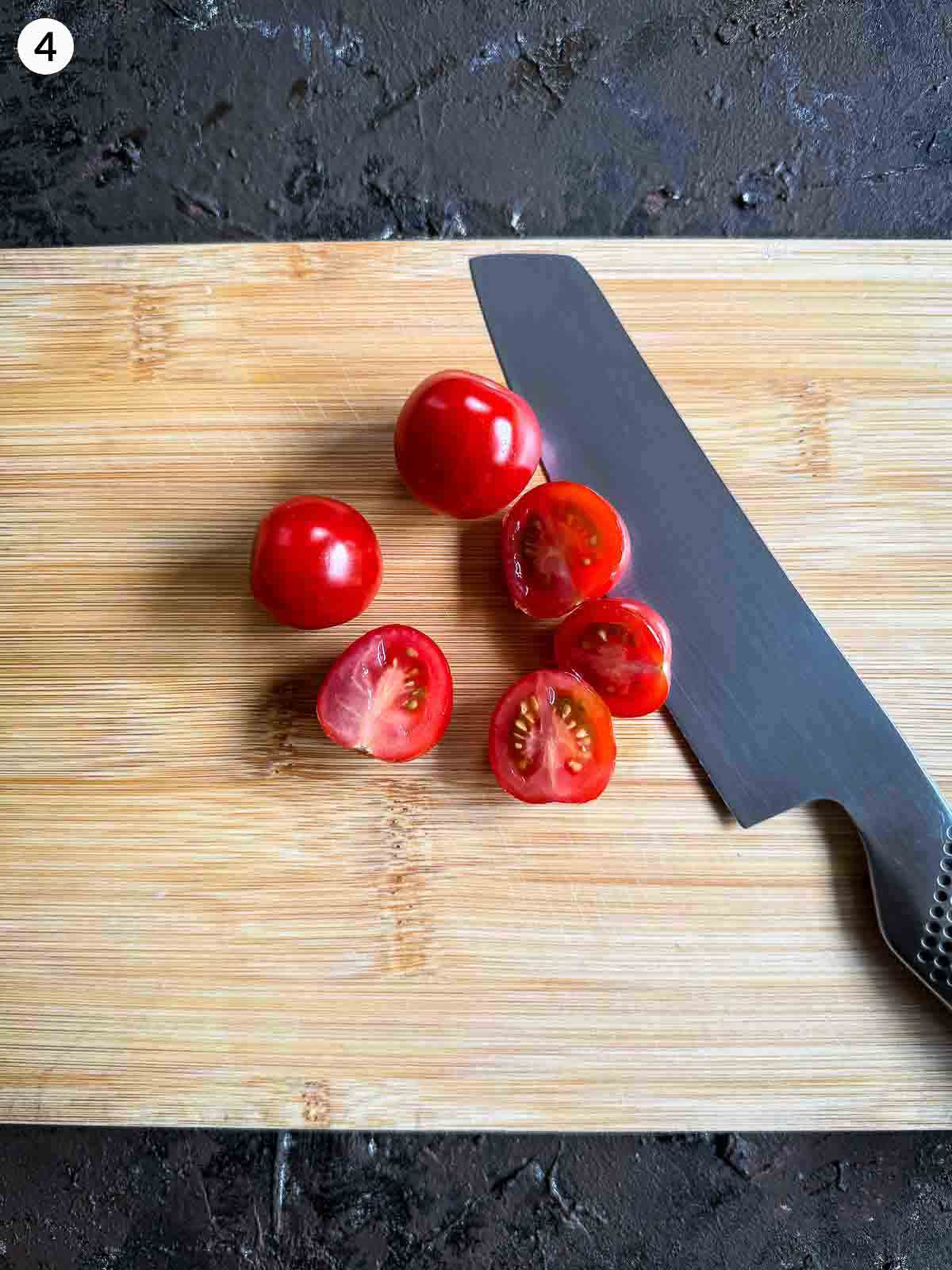 Halved cherry tomatoes on a wooden board beside a chef’s knife — preparing ingredients for baby corn salad.