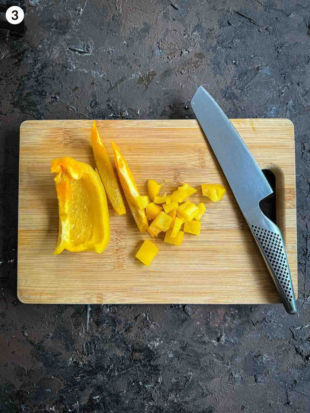 Chopping yellow capsicum on a wooden board — preparing vegetables for baby corn salad with parsnip crisps.