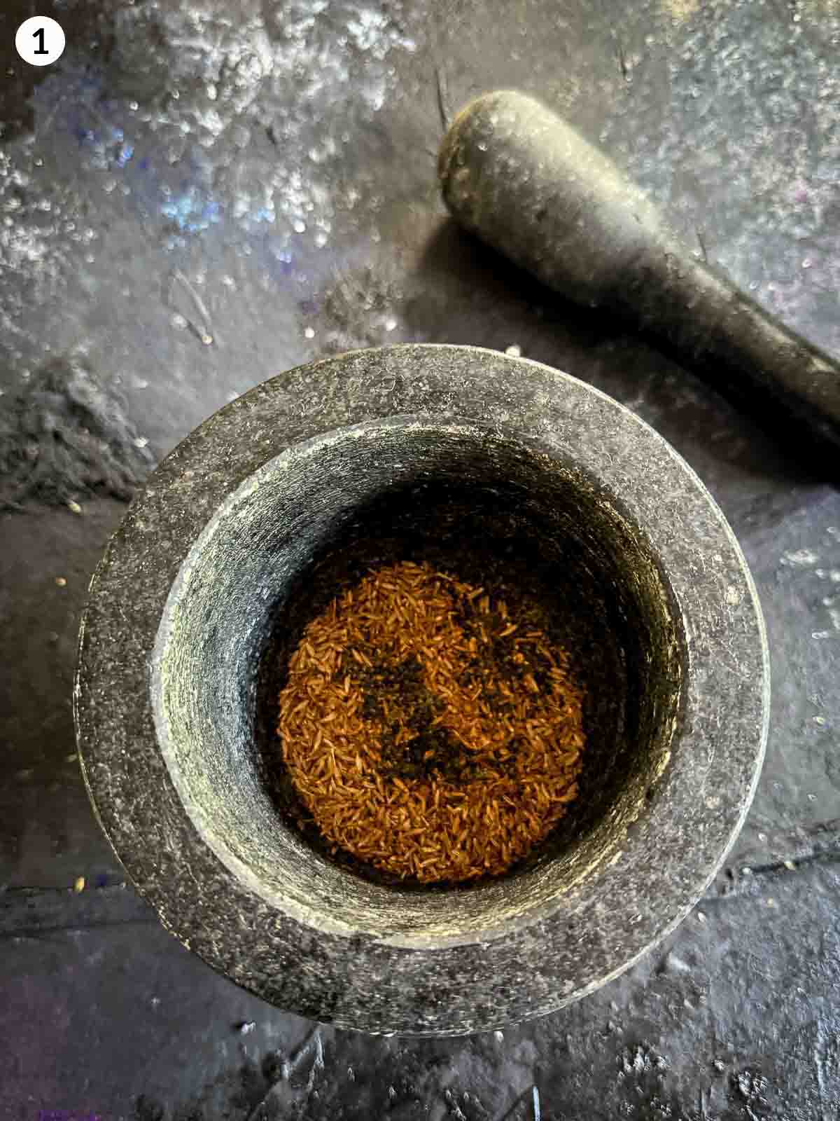 Ground cumin seeds in a mortar and pestle — preparing spice base for honey Greek yoghurt dressing in roasted cauliflower salad recipe.