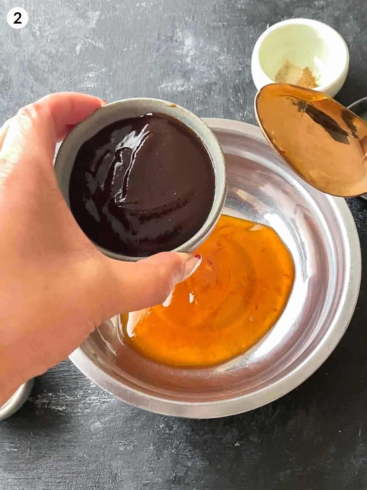 Adding hoi sin sauce into a bowl of plum sauce in a stainless steel bowl.