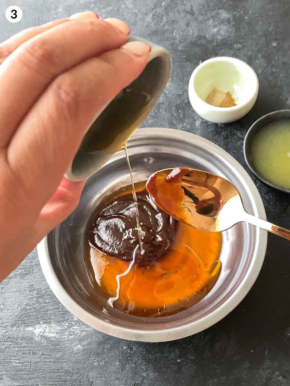 Adding sesame oil into a bowl of plum sauce and hoi sin sauce in a stainless steel bowl.
