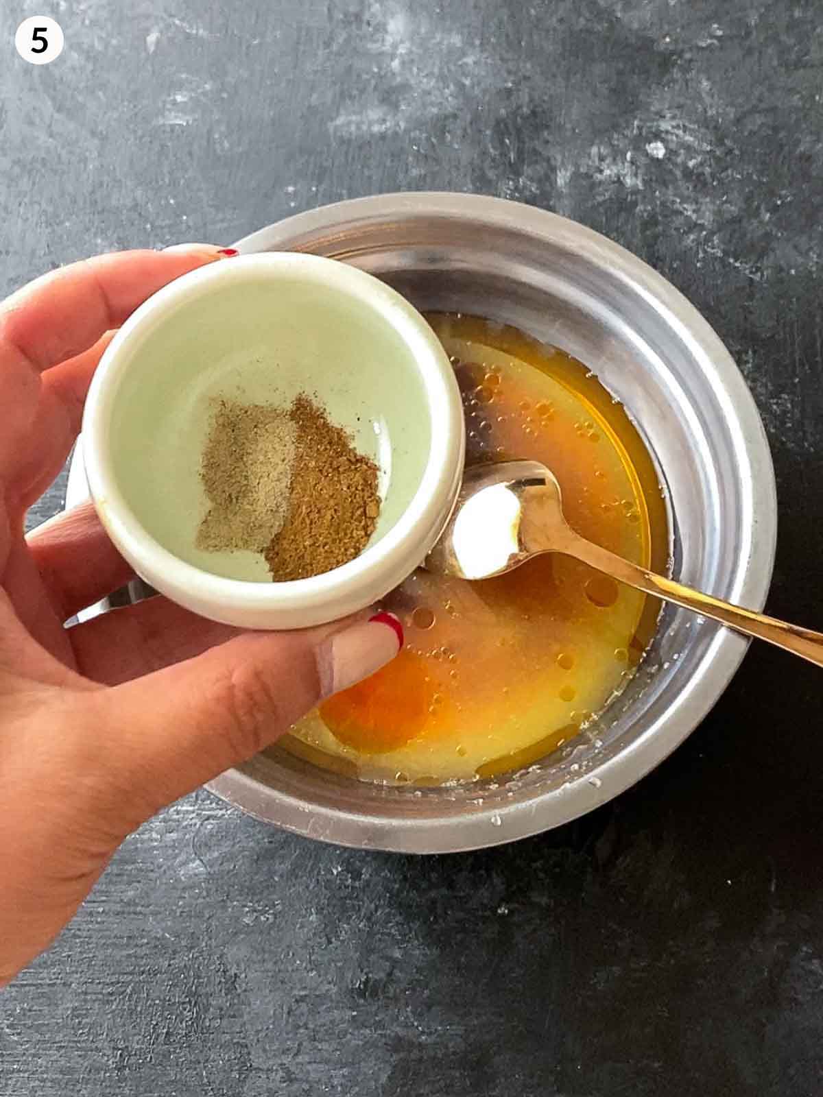 Adding pepper and five spice powder into a bowl of yee sang dressing in a stainless steel bowl