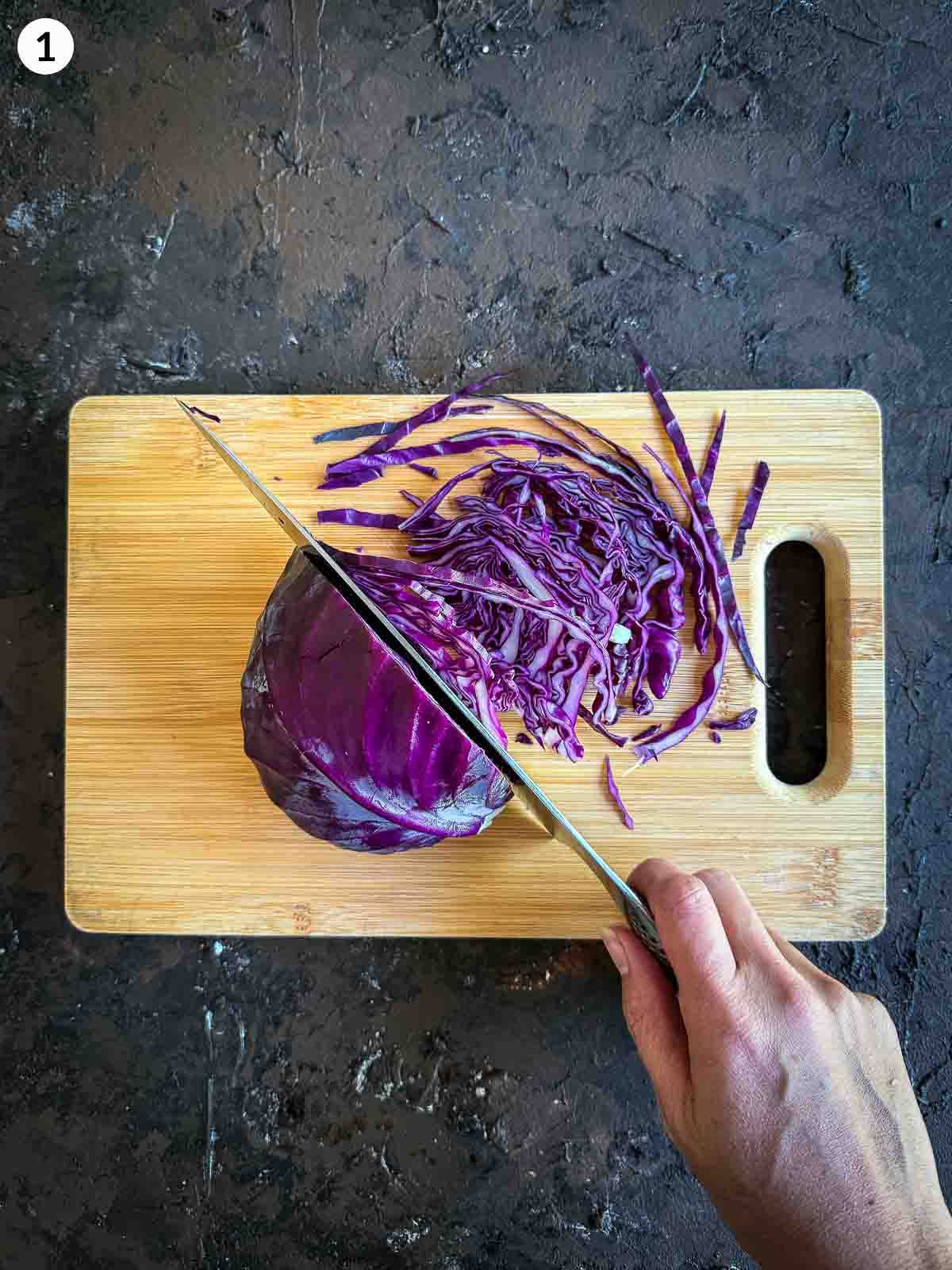 Slicing red cabbage finely on a wooden board — step to prepare crunchy cabbage for apple salad or side dish recipe.