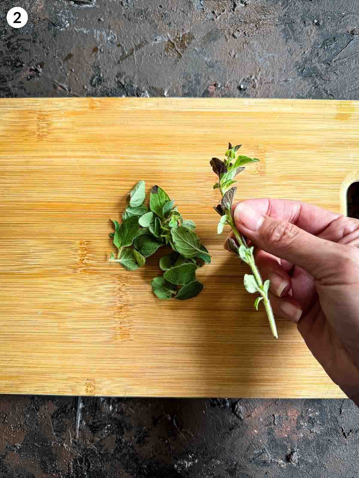 Hand picking fresh oregano leaves on a wooden board — adding herbs to baby corn salad with parsnip crisps.