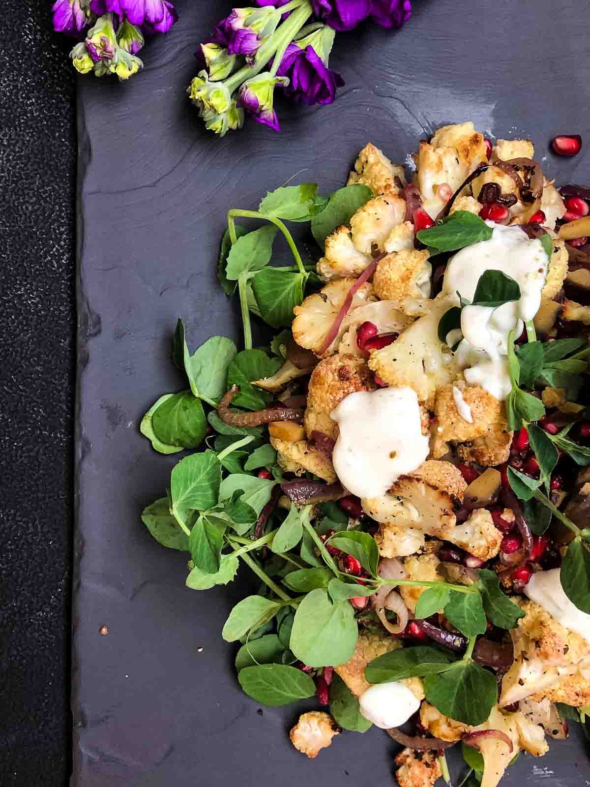 Vibrant oven roasted cauliflower salad with pomegranate seeds and greens, served as a healthy cauliflower side dish with honey Greek yogurt dressing.