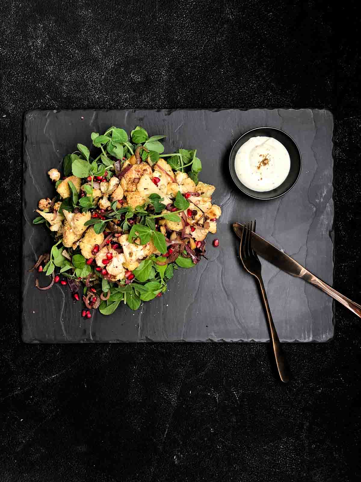 Image of roasted cauliflower salad topped with pomegranate and greens — an easy roasted cauliflower recipe with Greek yoghurt dressing.