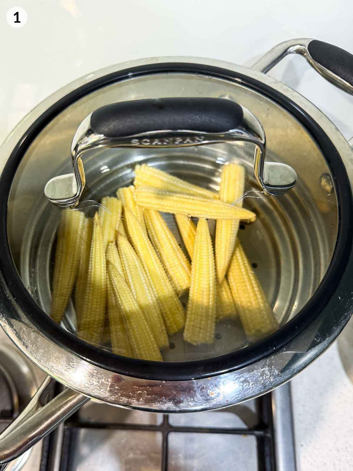 Baby corn steaming in a stainless-steel pot on the stove — preparation step for steamed corn salad and side dish with parsnip crisps.