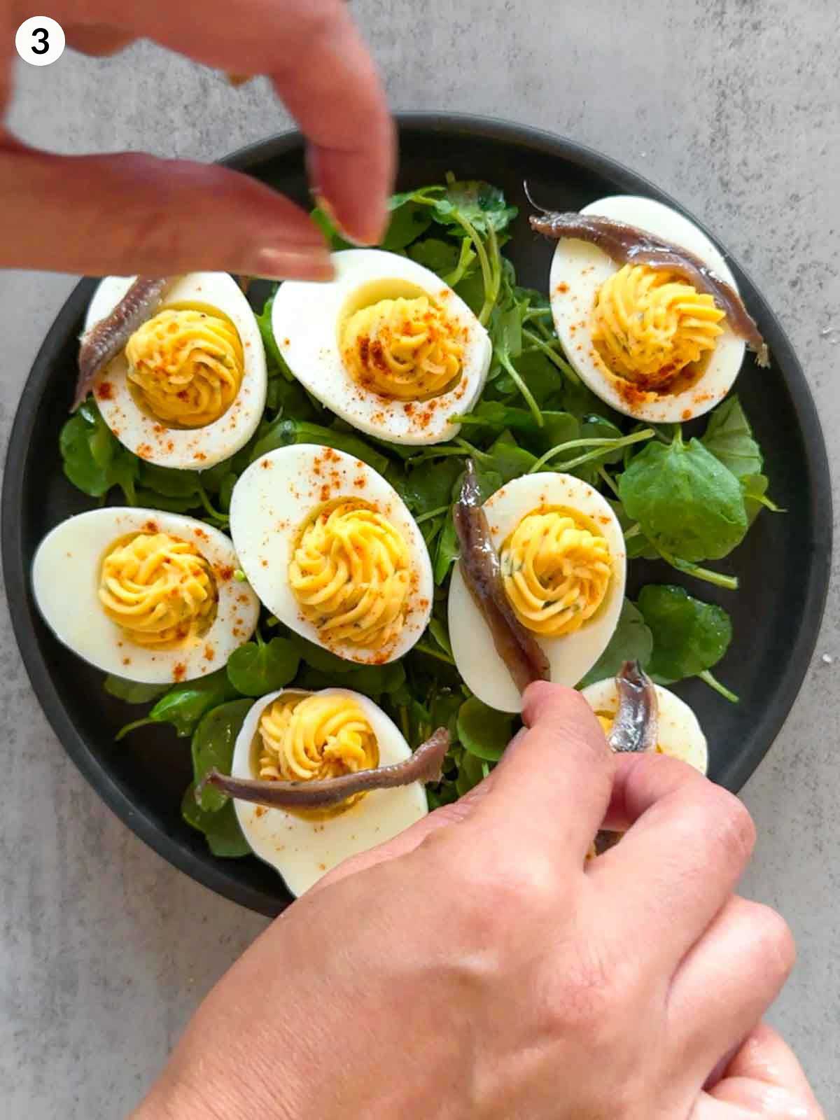 Adding anchovy fillets to deviled eggs served on a bed of watercress, finishing touches for a savoury and elegant make-ahead appetizer.