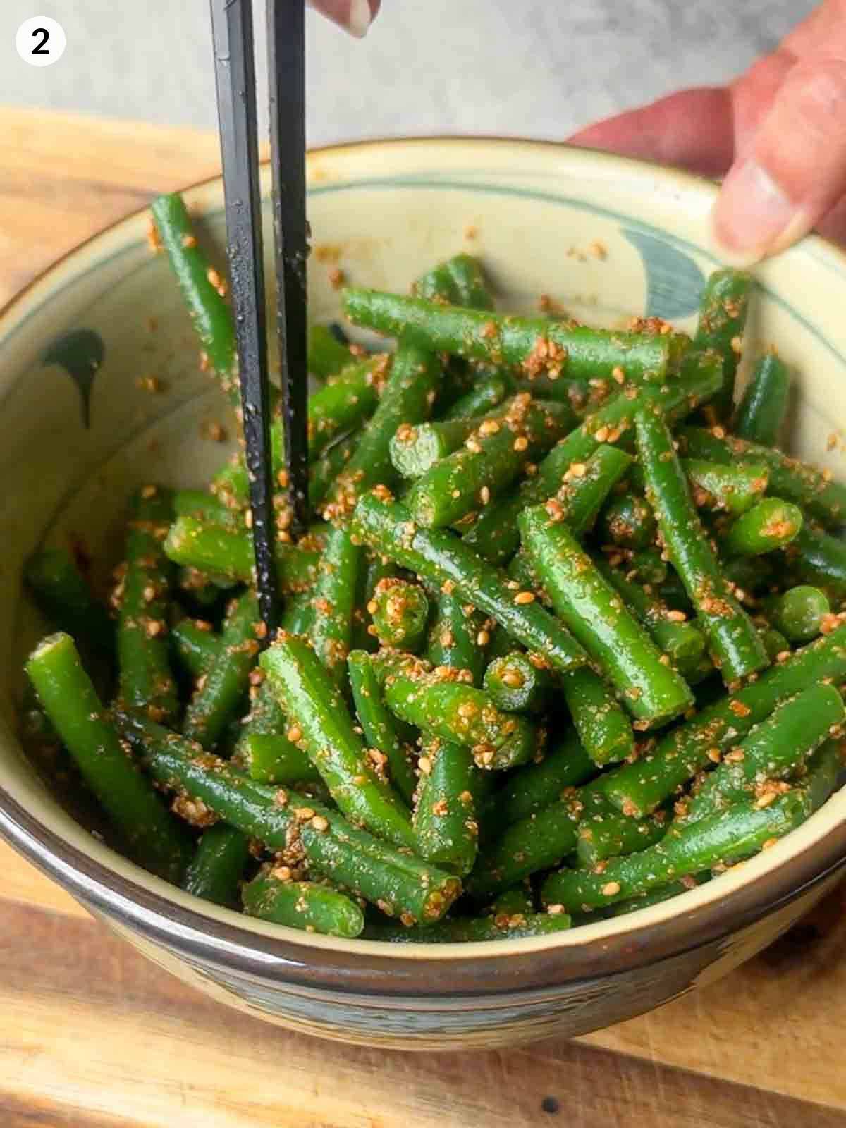 Adding rich gomae sesame sauce to blanched green beans in a ceramic bowl before mixing — a traditional Japanese side dish preparation.