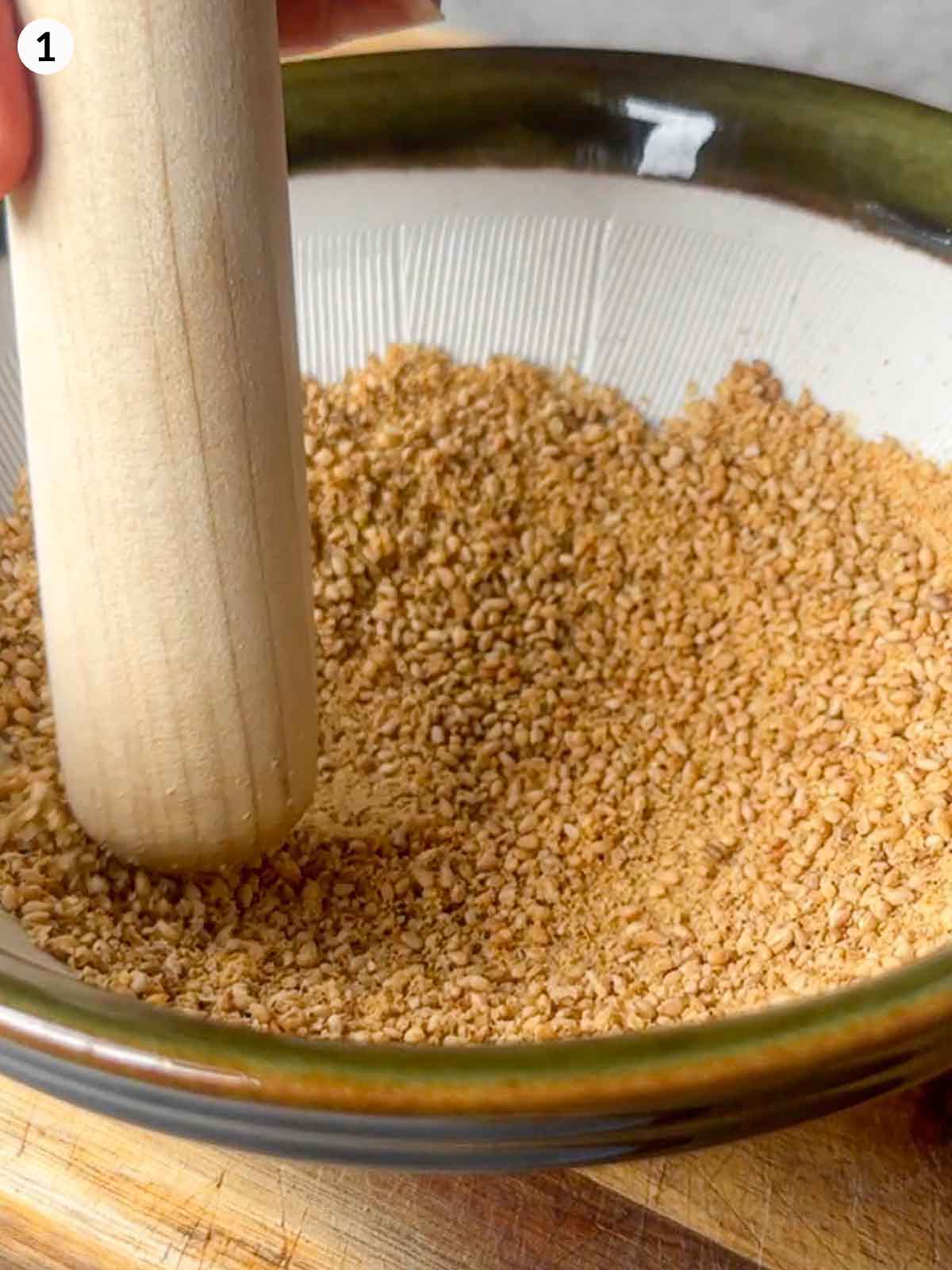 Grinding toasted sesame seeds in a traditional Japanese suribachi mortar with a wooden pestle to prepare the base for gomae sesame sauce.
