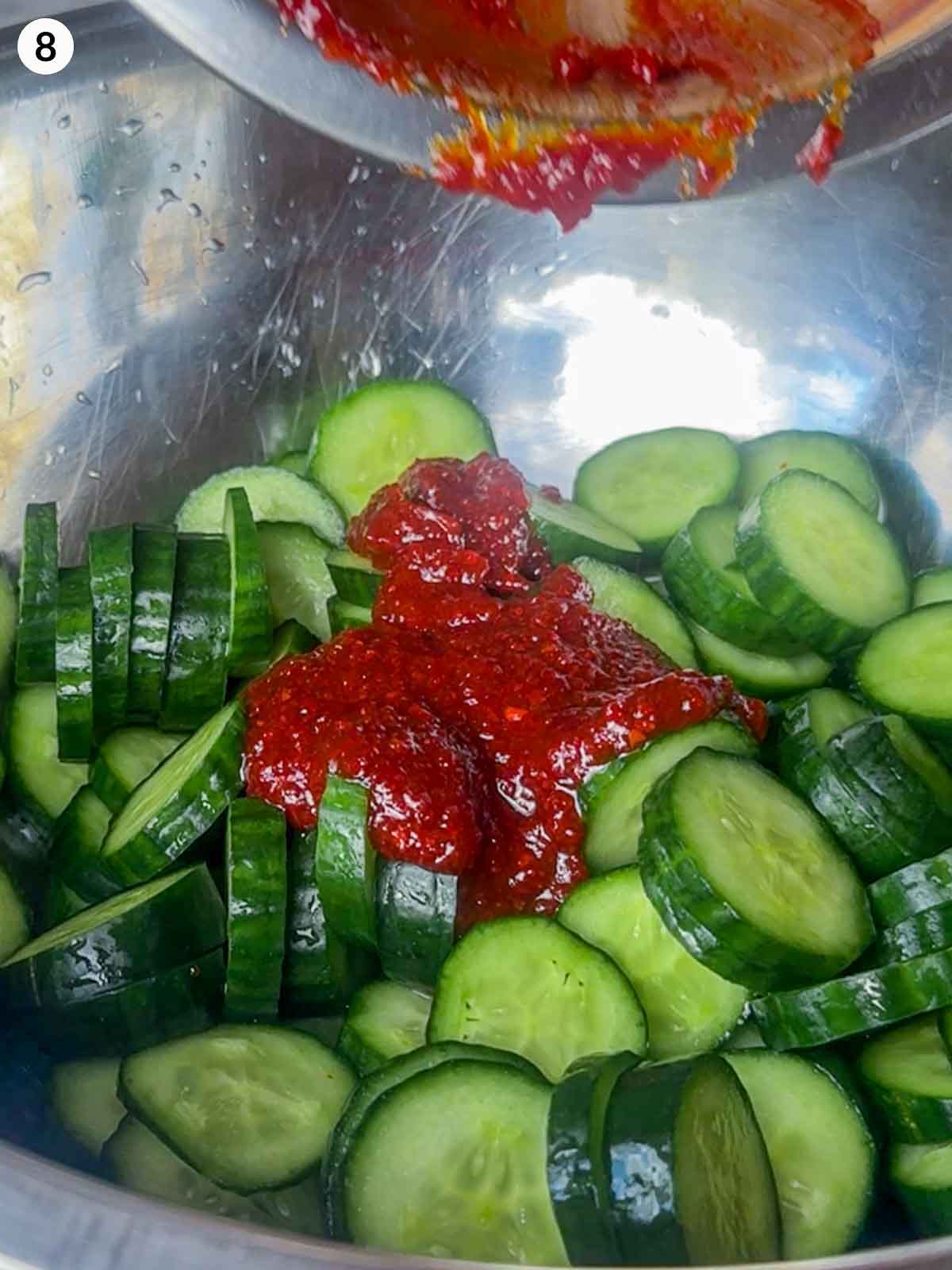 Sliced cucumbers in a bowl topped with red gochugaru chili paste mixture for spicy cucumber kimchi (Oi Kimchi).