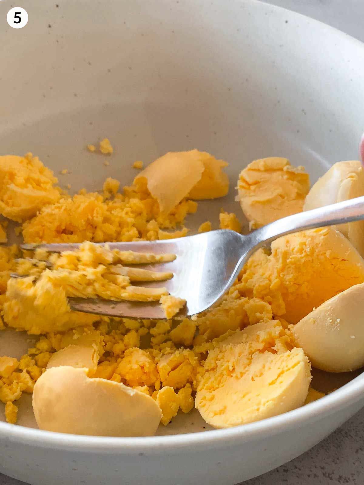Smashing egg yolks with a fork in a white bowl