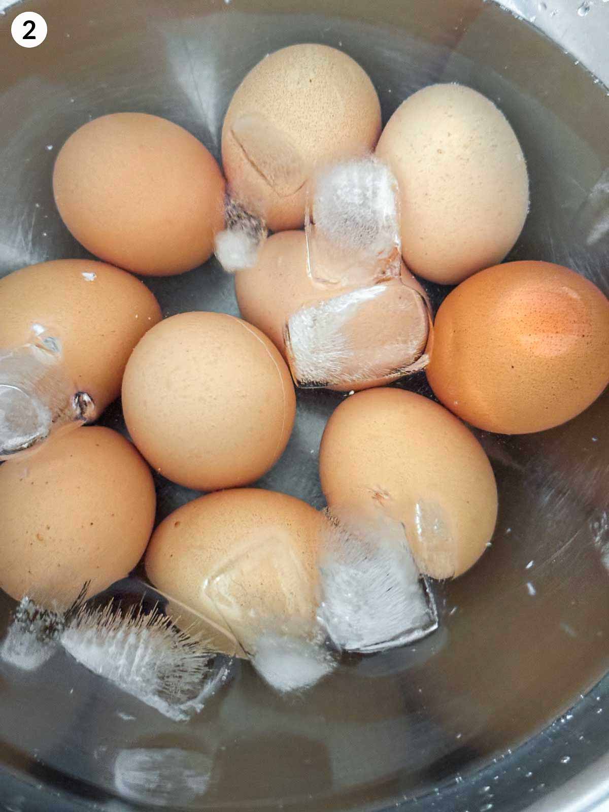 Boiled eggs cooling in a stainless steel bowl filled with ice water to stop the cooking process — the perfect step for making easy peel eggs for deviled egg recipes.