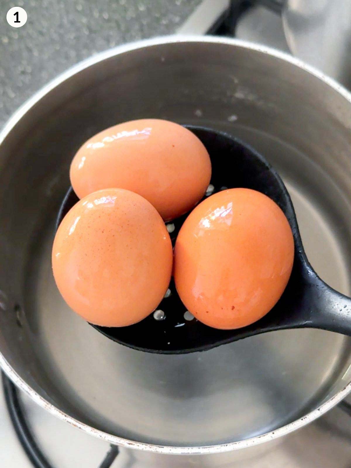 Adding eggs in a slotted spoon into a pot of water