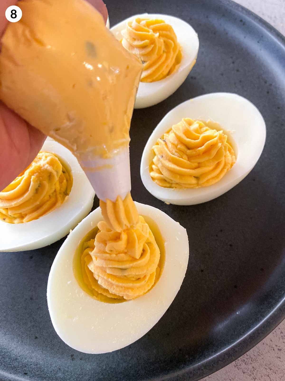 Piping creamy deviled egg filling into halved egg whites using a piping bag, creating neat swirls of smooth yolk mixture for a classic deviled egg recipe.