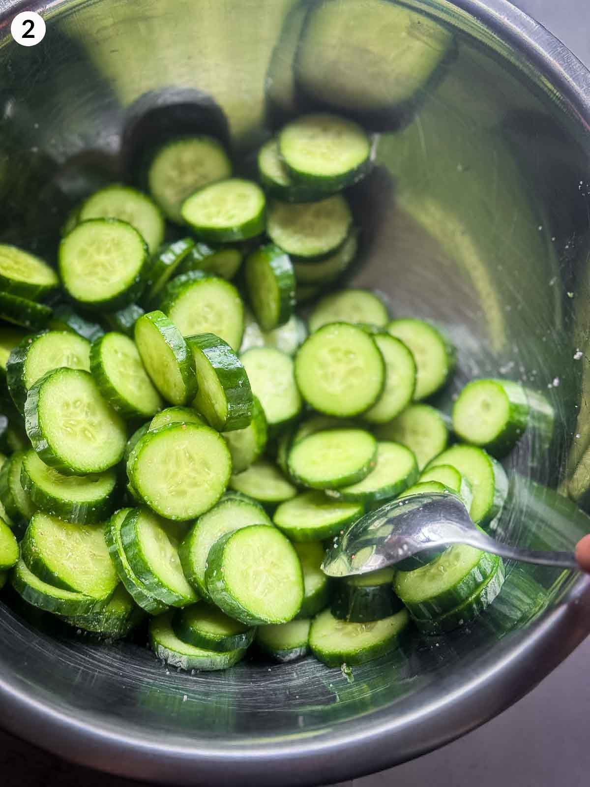 Cucumber slices being salted in a metal bowl — step one in making spicy Korean cucumber kimchi (Oi Kimchi).
