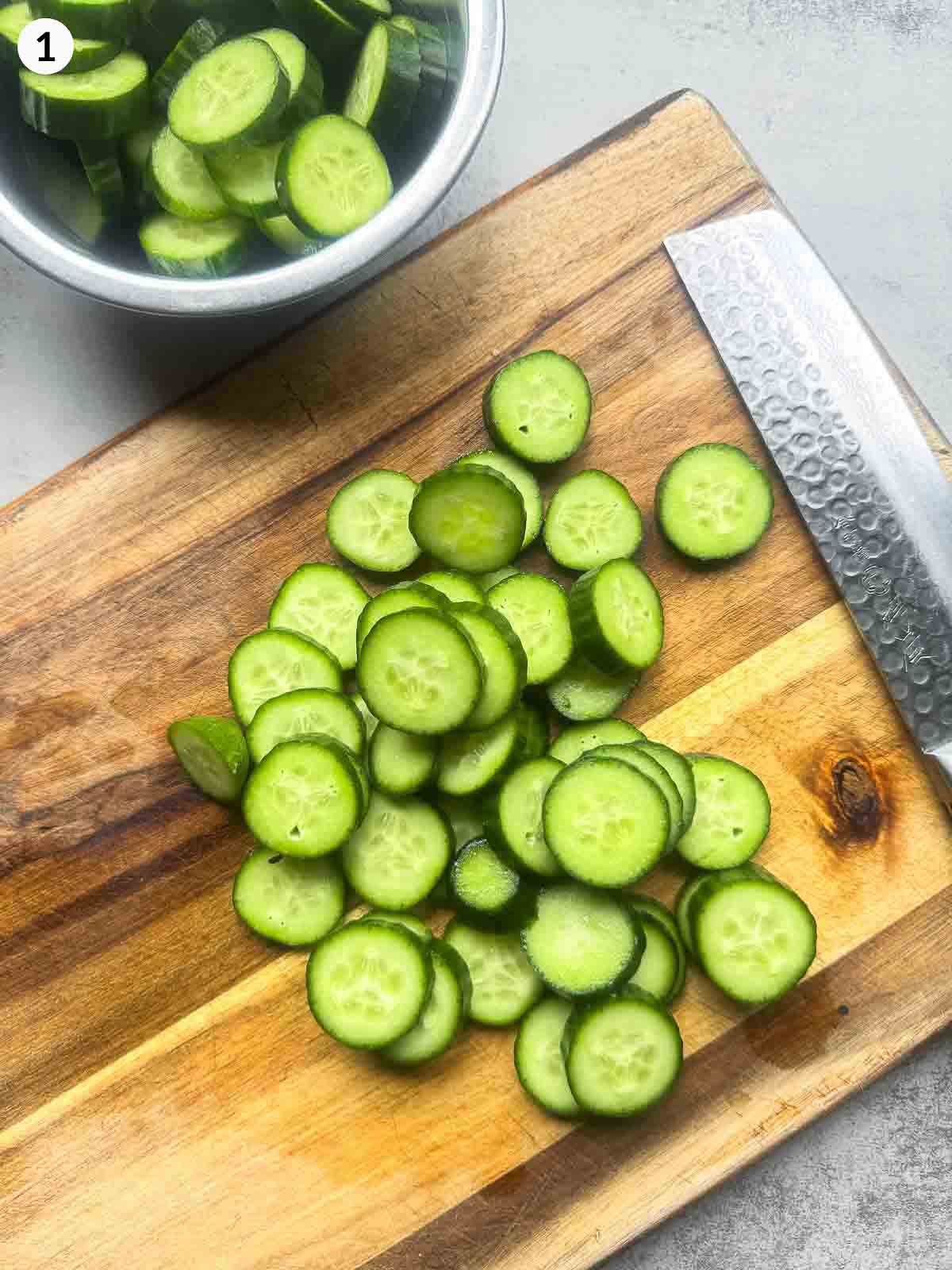 Sliced cucumbers on a wooden board beside a knife, ready to be seasoned for Korean cucumber kimchi (Oi Kimchi).