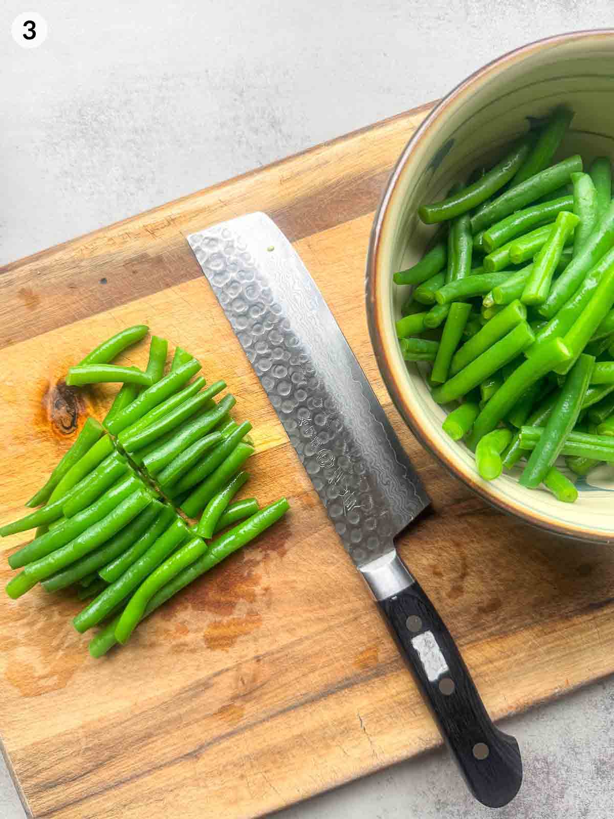 Cutting blanched green beans into bite-sized pieces on a wooden board before mixing with sesame sauce — prepping for Japanese green bean Gomaae.
