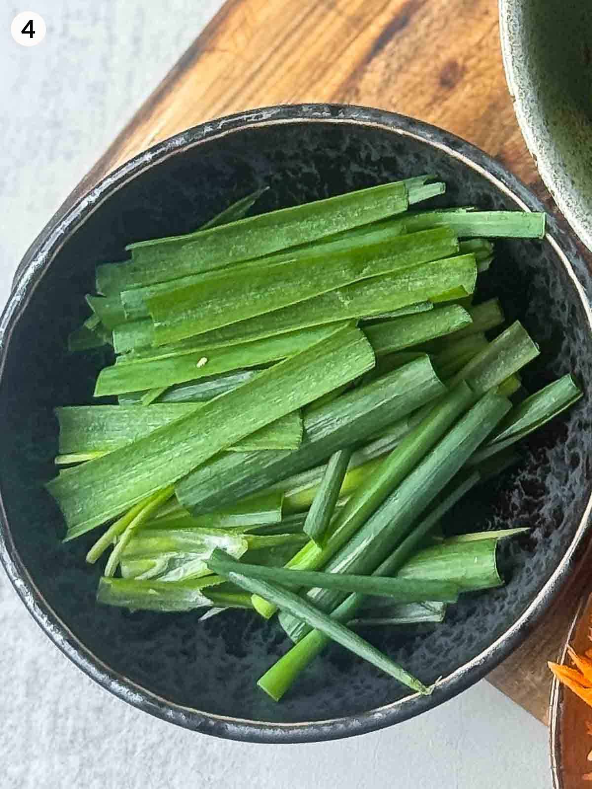 Freshly cut scallions (green onions) in a small black bowl, ready to be added to spicy cucumber kimchi (Oi Kimchi).