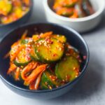 Bowls of Korean cucumber kimchi (Oi Kimchi) with sliced cucumber, carrot, and sesame seeds in a spicy red chili paste — a simple, vibrant Korean side dish.