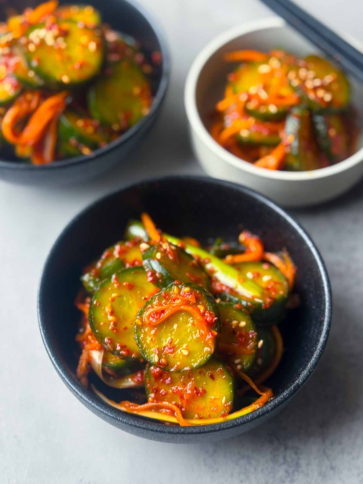 Bowls of Korean cucumber kimchi (Oi Kimchi) with sliced cucumber, carrot, and sesame seeds in a spicy red chili paste — a simple, vibrant Korean side dish.