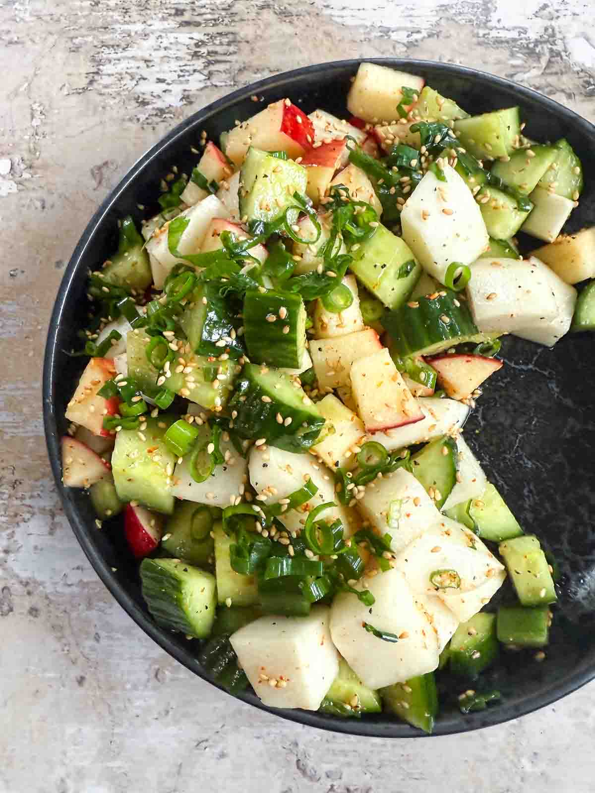 Daikon Cucumber Apple Salad with Togarashi Dressing on a black plate