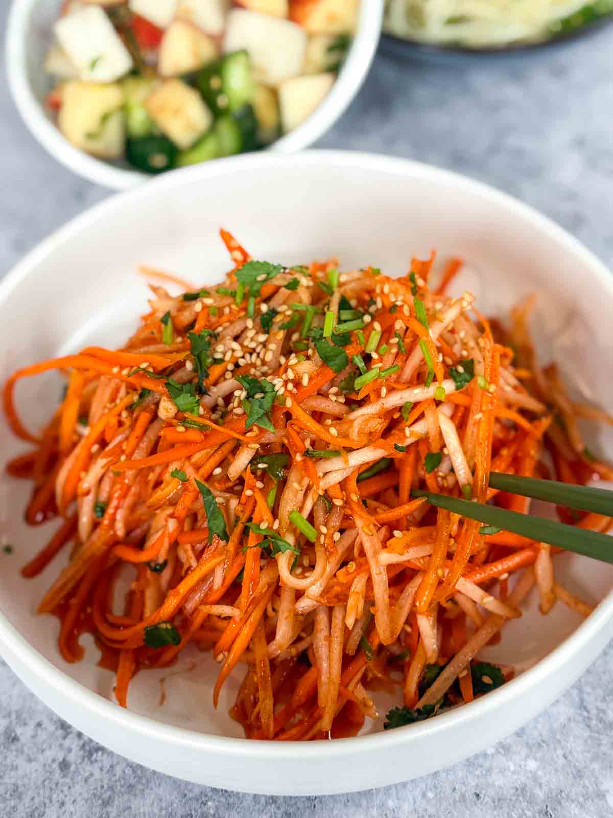 Bowl of Carrot and Daikon Salad with green chopsticks served with another salad and some egg noodles