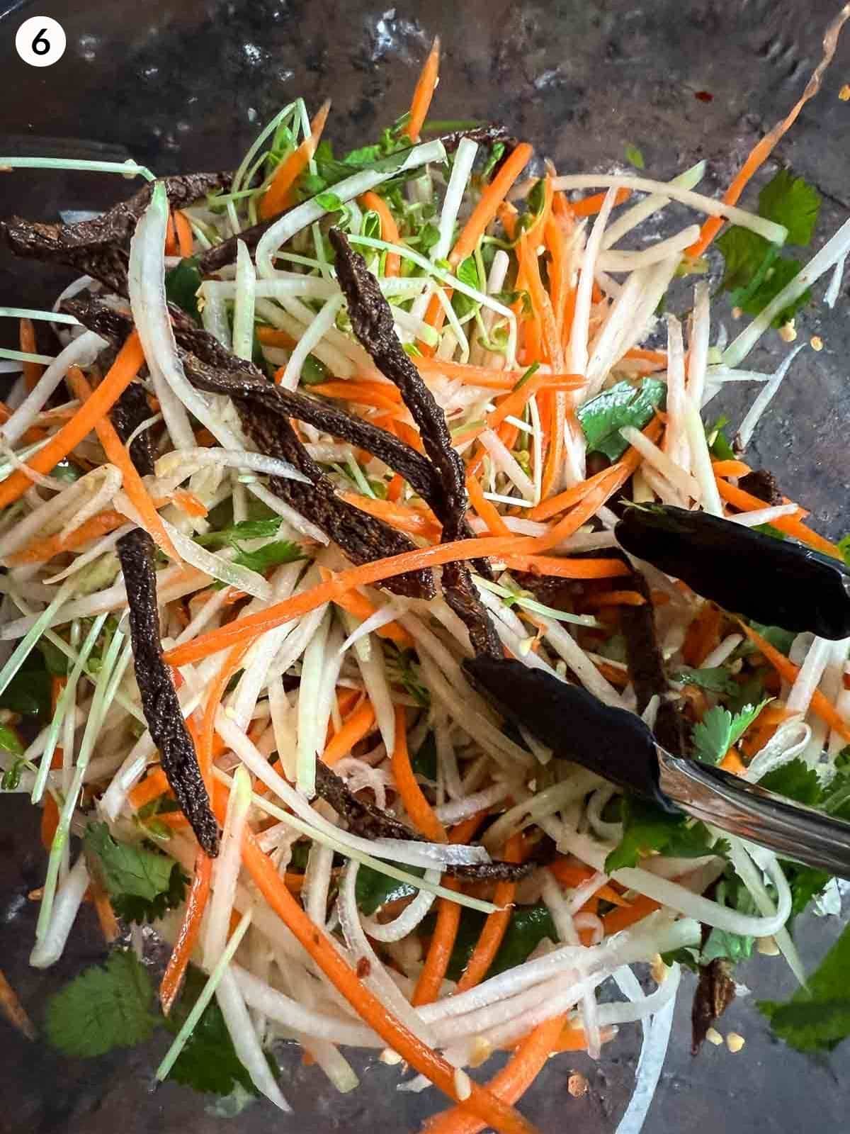 Mixing the ingredients of Asian Slaw Recipe with Beef Jerky and Kohlrabi ingredients in a clear mixing bowl
