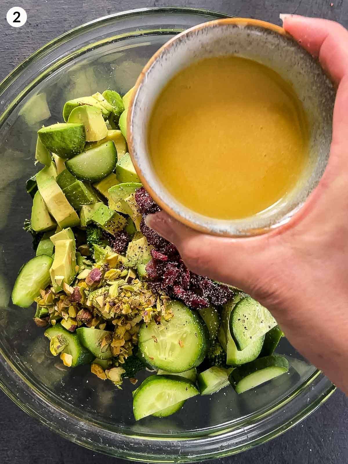 Hand holding a bowl of salad dressing to pour into a mixing bowl of Cranberry and Kale salad ingredients