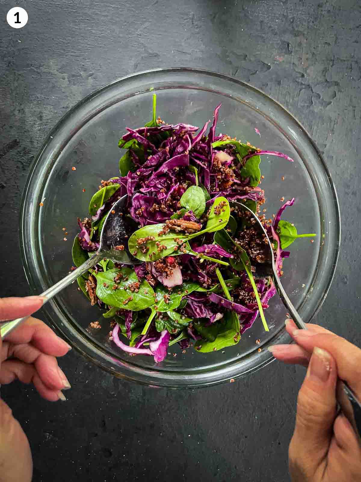 Tossing Quinoa Pumpkin Salad ingredients in a clear mixing bowl with 2 large soons