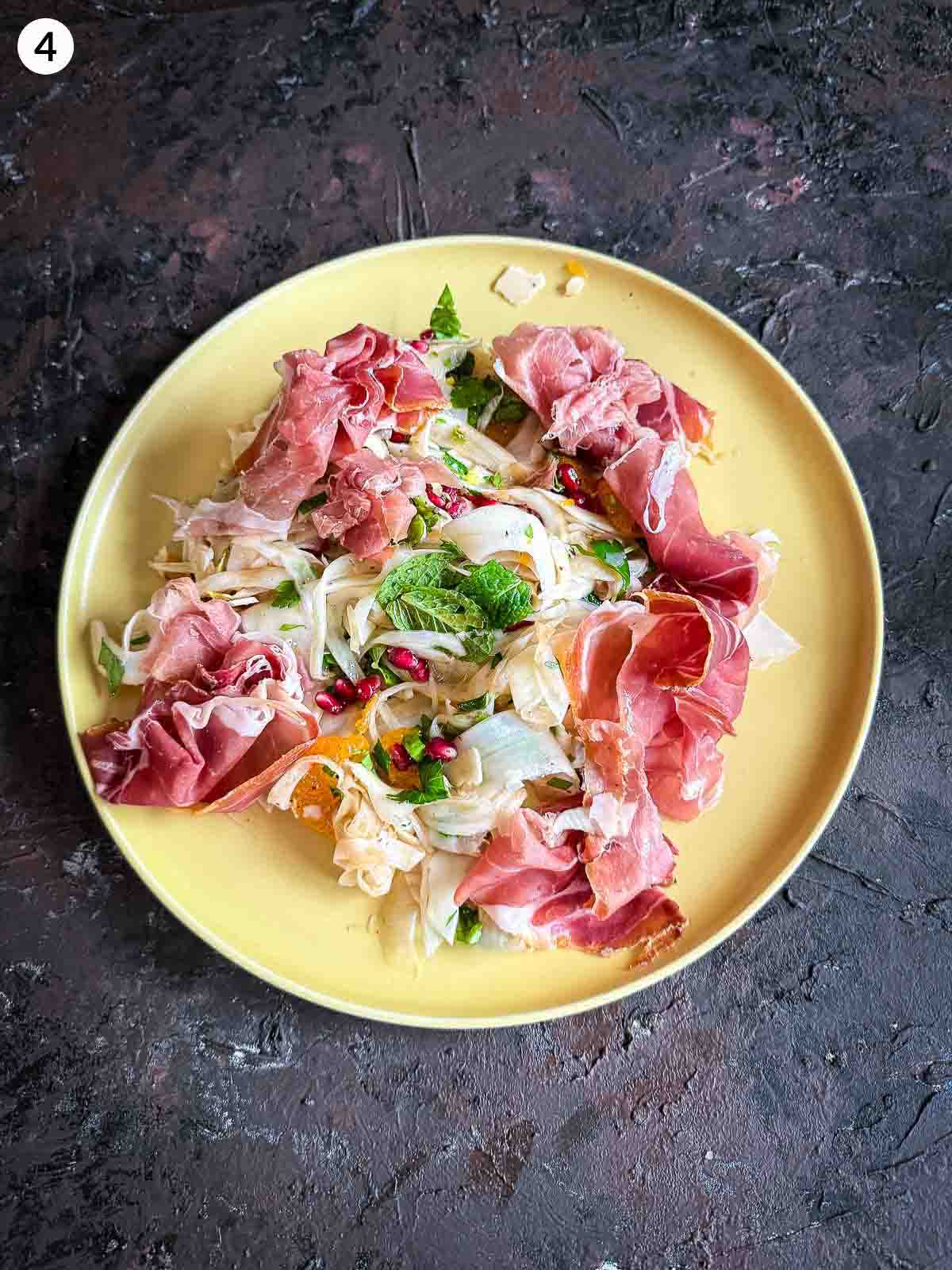 Assembling ingredients for Shaved Fennel Salad with Mandarin, Prosciutto & Pomegranate in a yellow plate
