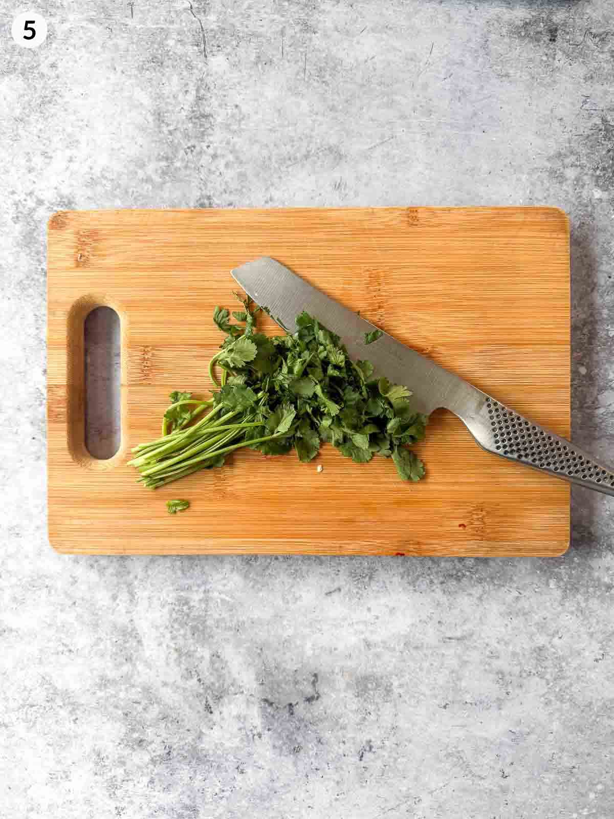 Roughly chopping coriander leaves with a knife on a wooden chopping board