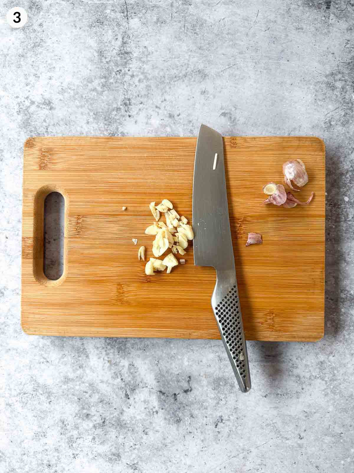 Cutting garlic with a knife on a wooden chopping board