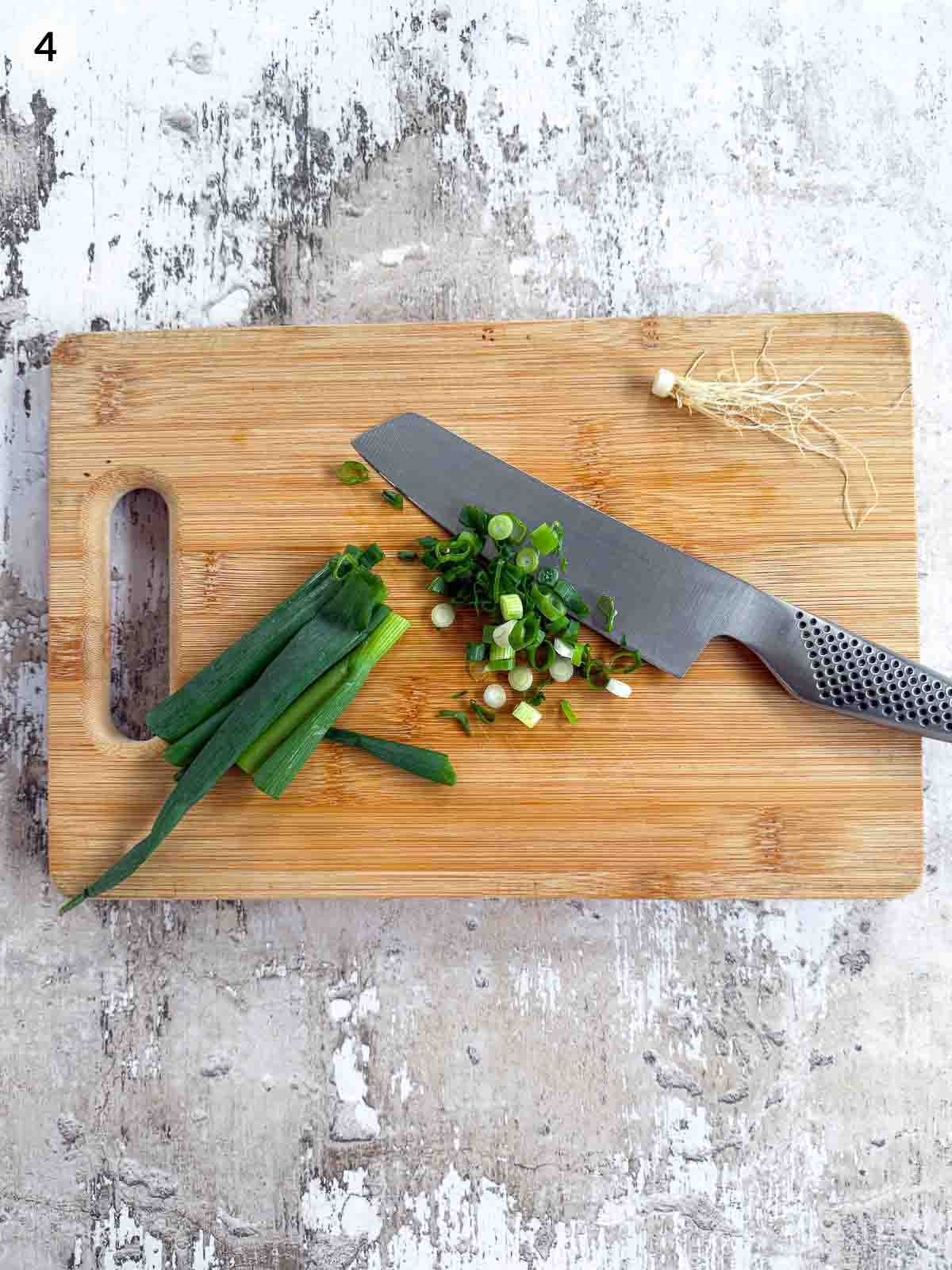Cutting spring onion with a knife on a wooden chopping board