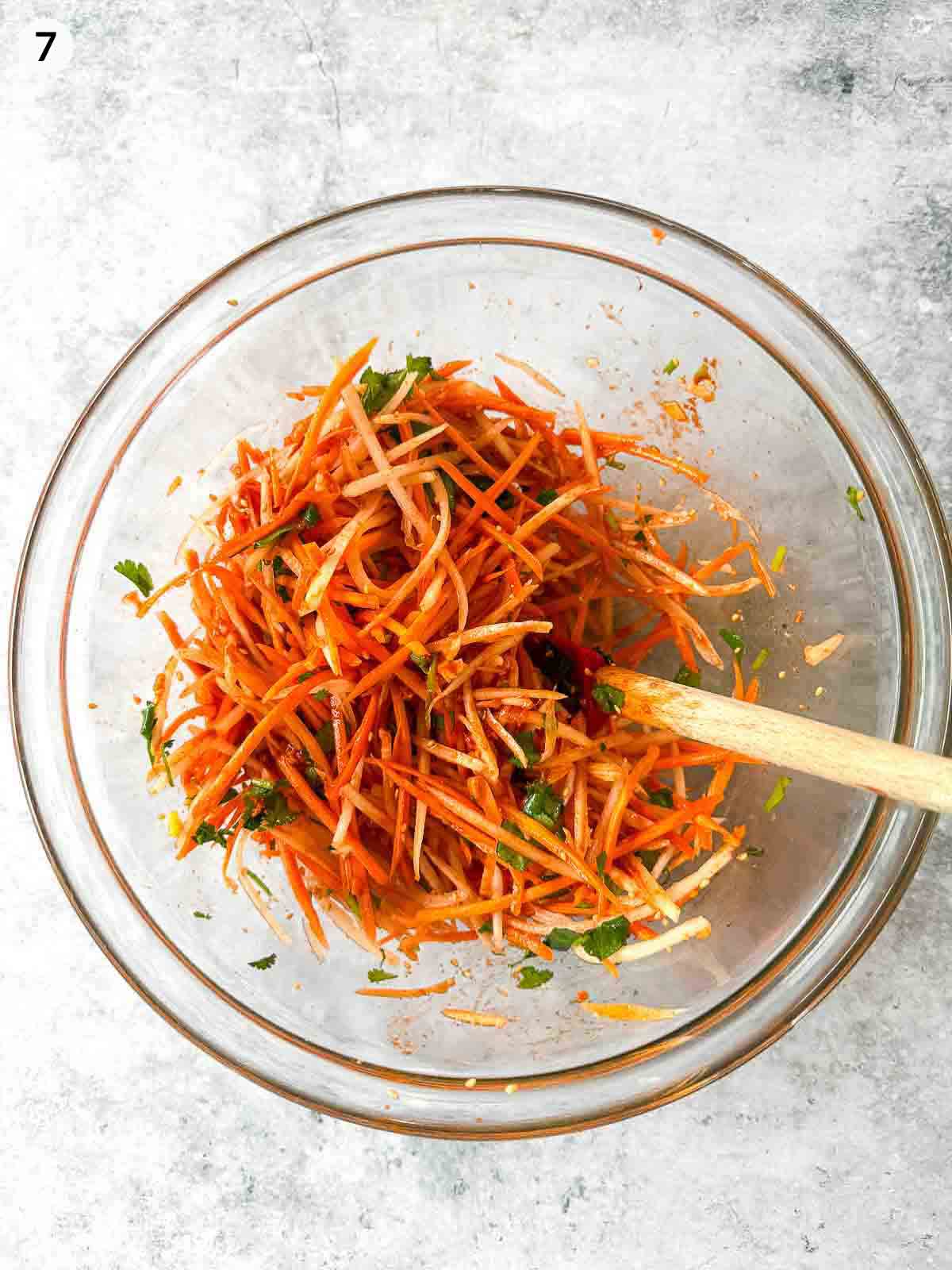 Mixing ingredients for Carrot and Daikon Salad in a clear bowl