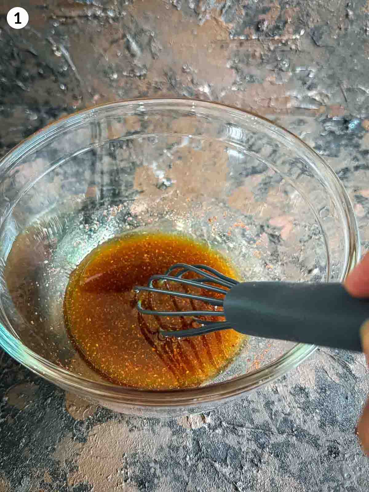 Mixing ingredients for honey orange salad dressing with a whisk in a clear bowl