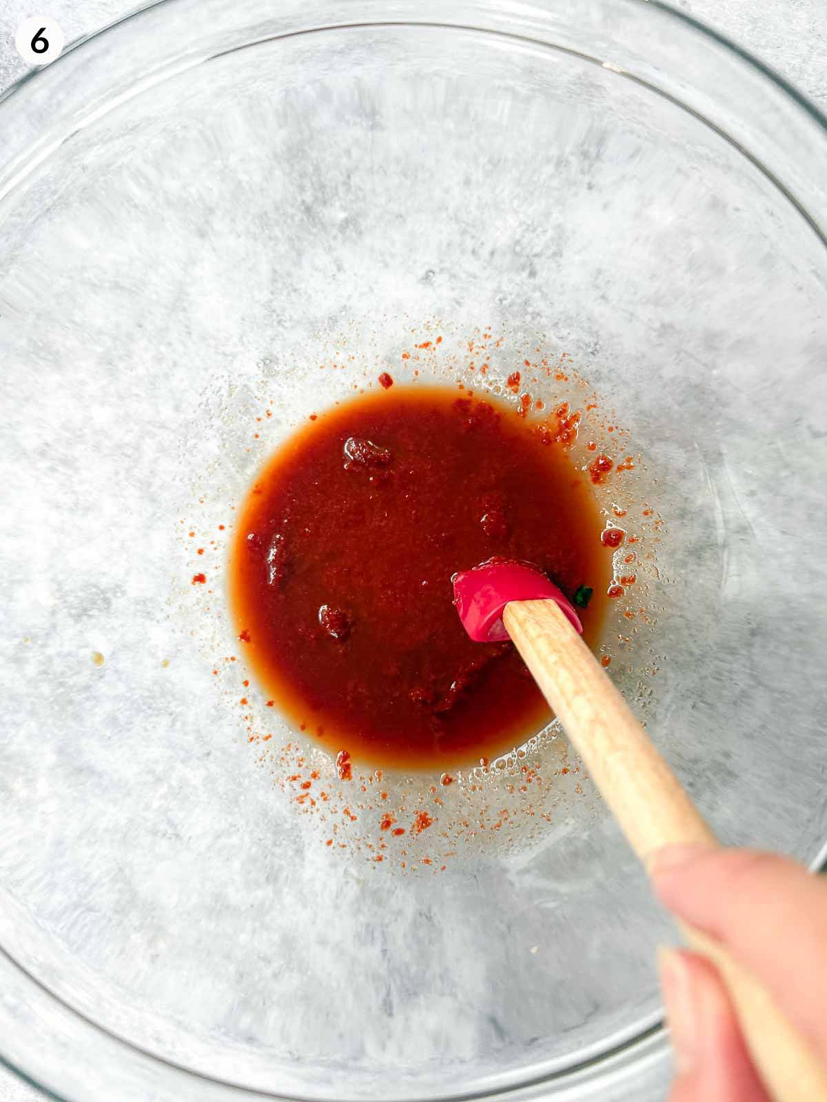 Mixing gochujang salad dressing in a clear mixing bowl with a small red spatula