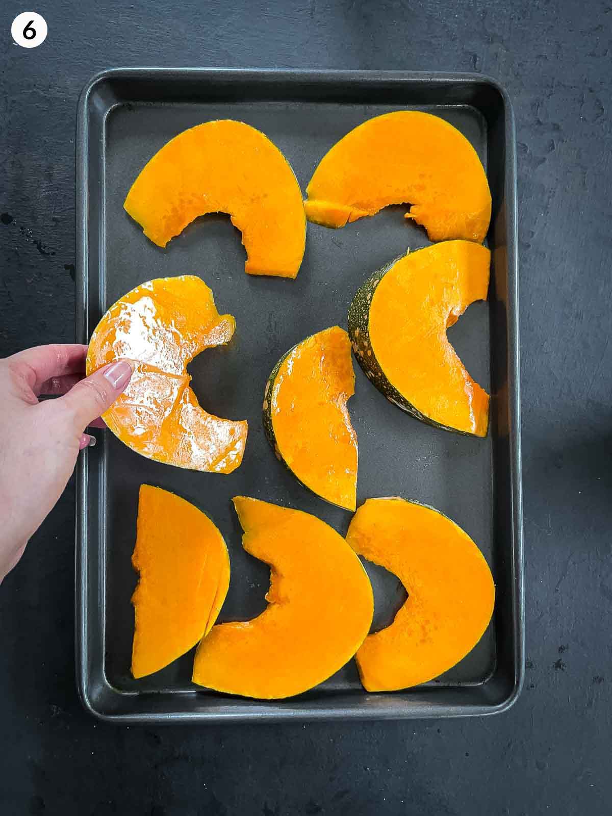 Placing wedges of kent pumpkin on a sheet pan against a dark background