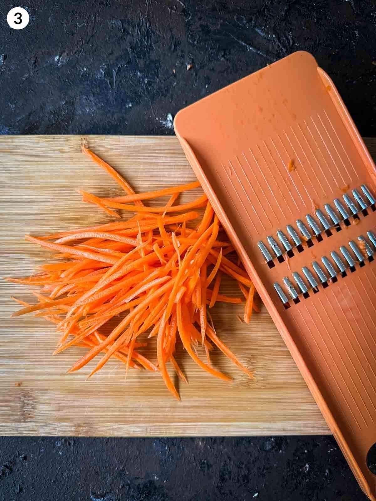 Shredding carrot with a mandoline on a wooden chopping board on a dark background