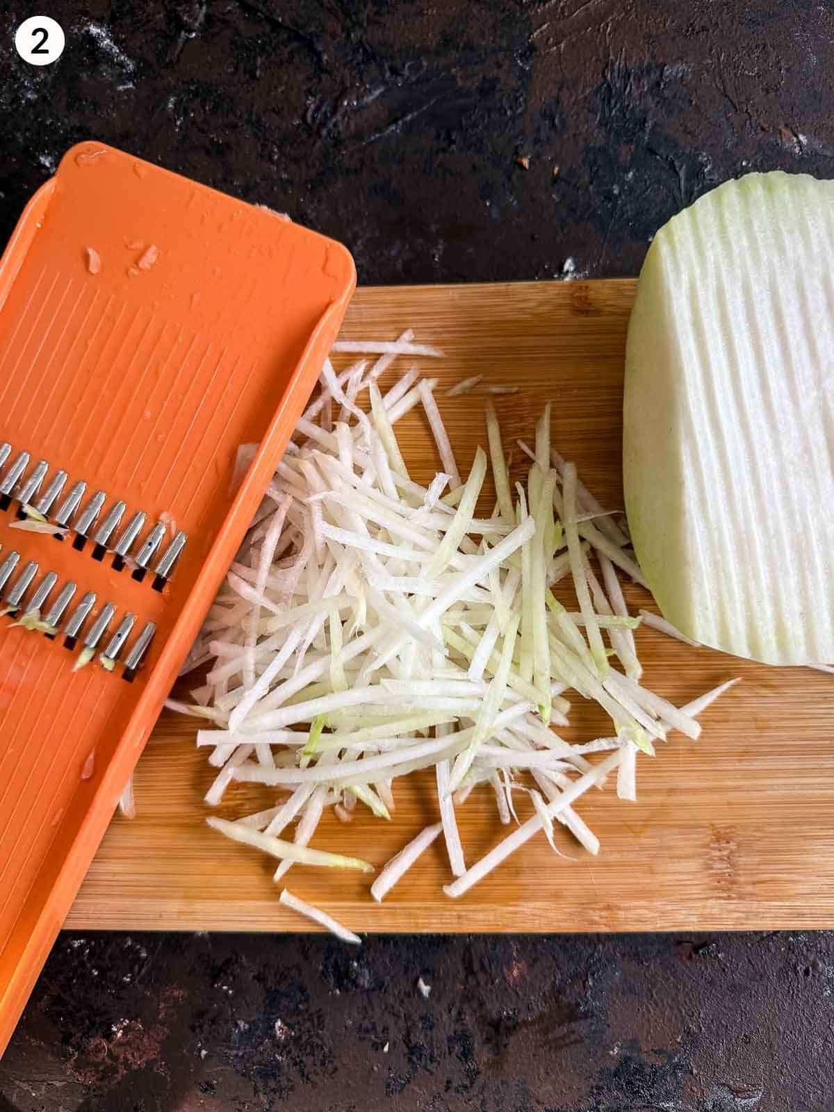 Shredding kohlrabi with a mandoline on a wooden chopping board on a dark background