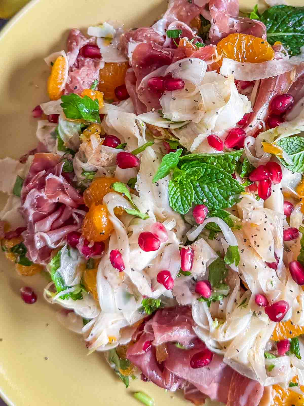 Shaved Fennel Salad with Mandarin, Prosciutto & Pomegranate served on a yellow plate