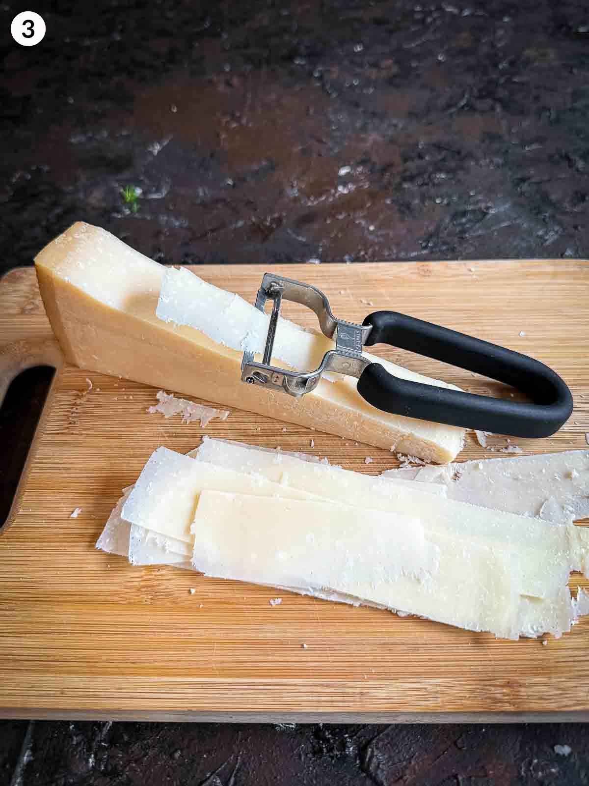 shaving parmigiano Reggiano cheese with a wide mouth peeler on a wooden board
