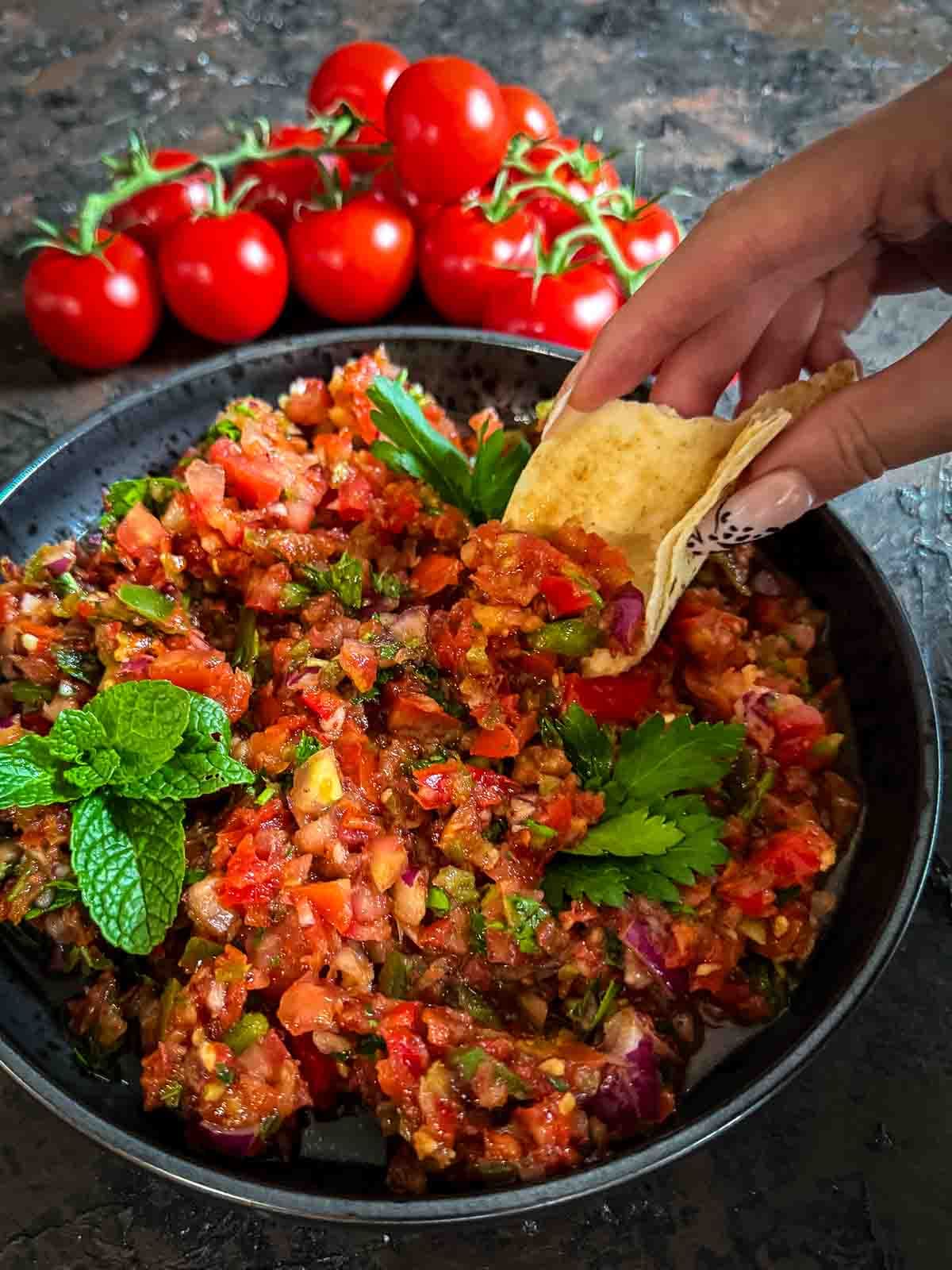 Bowl of Turkish ezme salad in a black plate served with Lebanese bread and truss tomatoes in the background