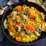 Saffron Israeli Couscous with Roasted Artichoke Hearts in a cast iron pan with blue napkins and cutlery on the side