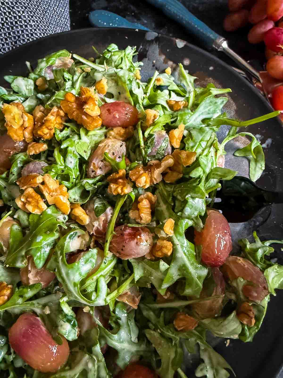 Warm Arugula and Roasted Grape Salad with Blue Cheese served on a dark plate with blue serving cutlery and fresh red grapes on the side