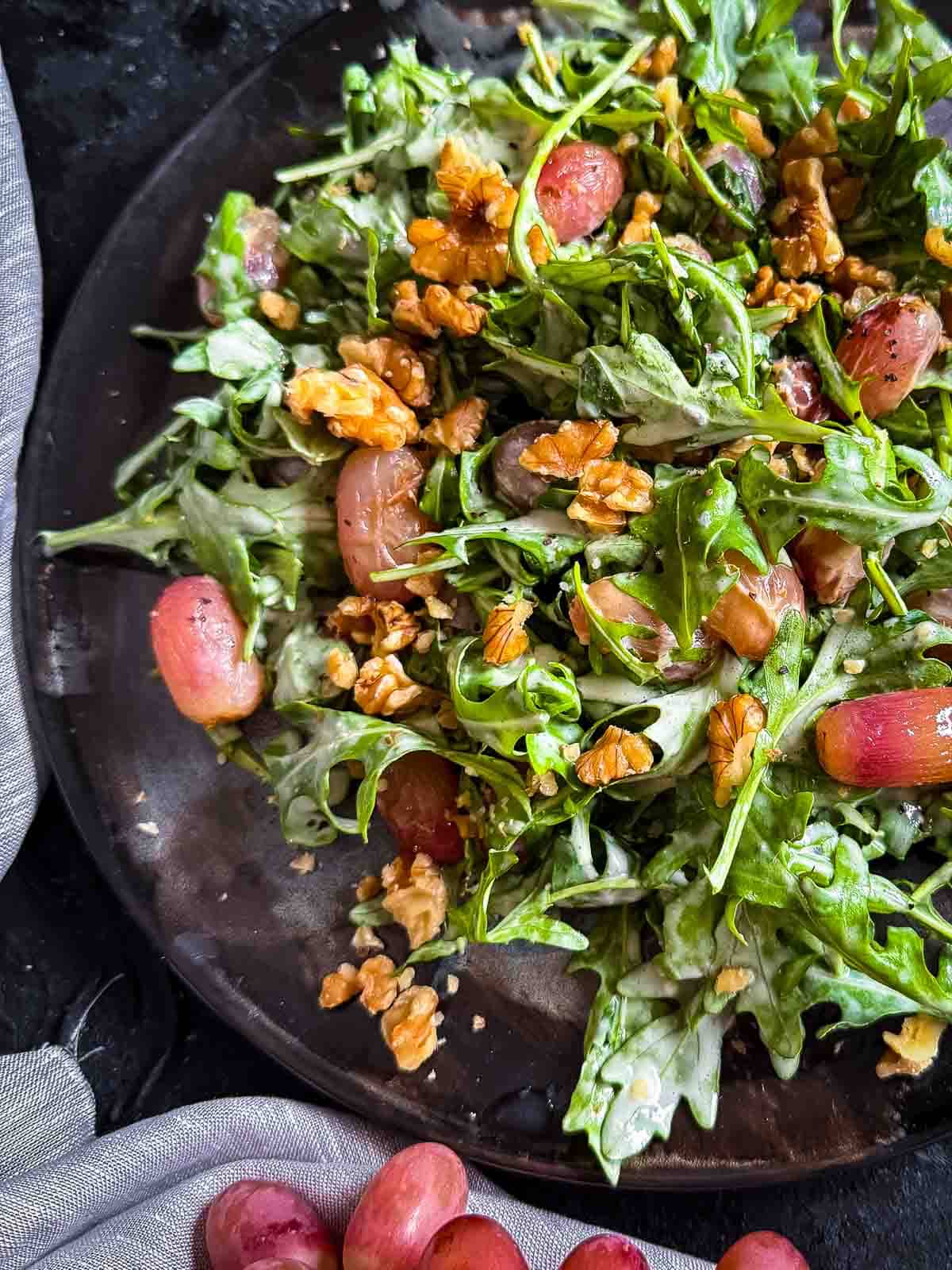 Warm Arugula and Roasted Grape Salad with Blue Cheese served on a dark plate with grey linen and fresh grapes on the side