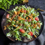 Warm Arugula and Roasted Grape Salad with Blue Cheese served on a dark plate with gold serving cutlery and fresh arugula on the side