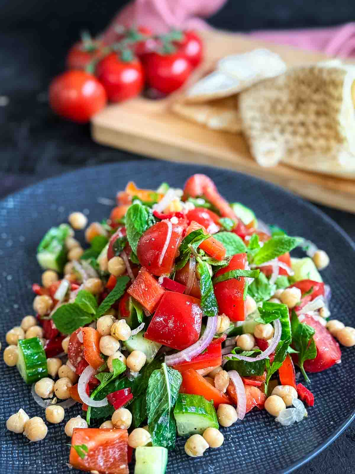 Balela Salad on a blue plate with flat bread and tomatoes on a wooden board in the background