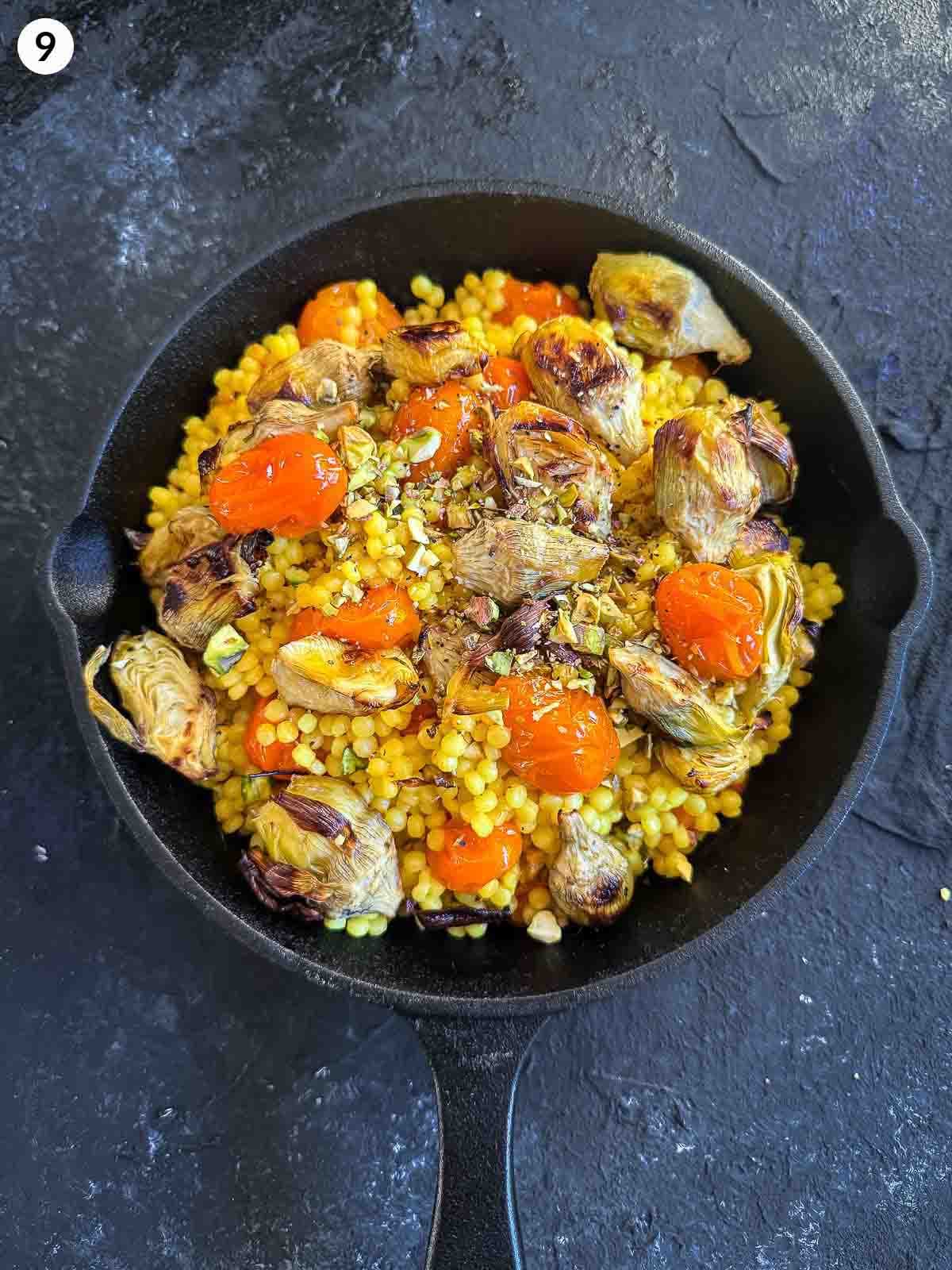 assembling Saffron Israeli Couscous with Roasted Artichoke Hearts in a cast iron pan