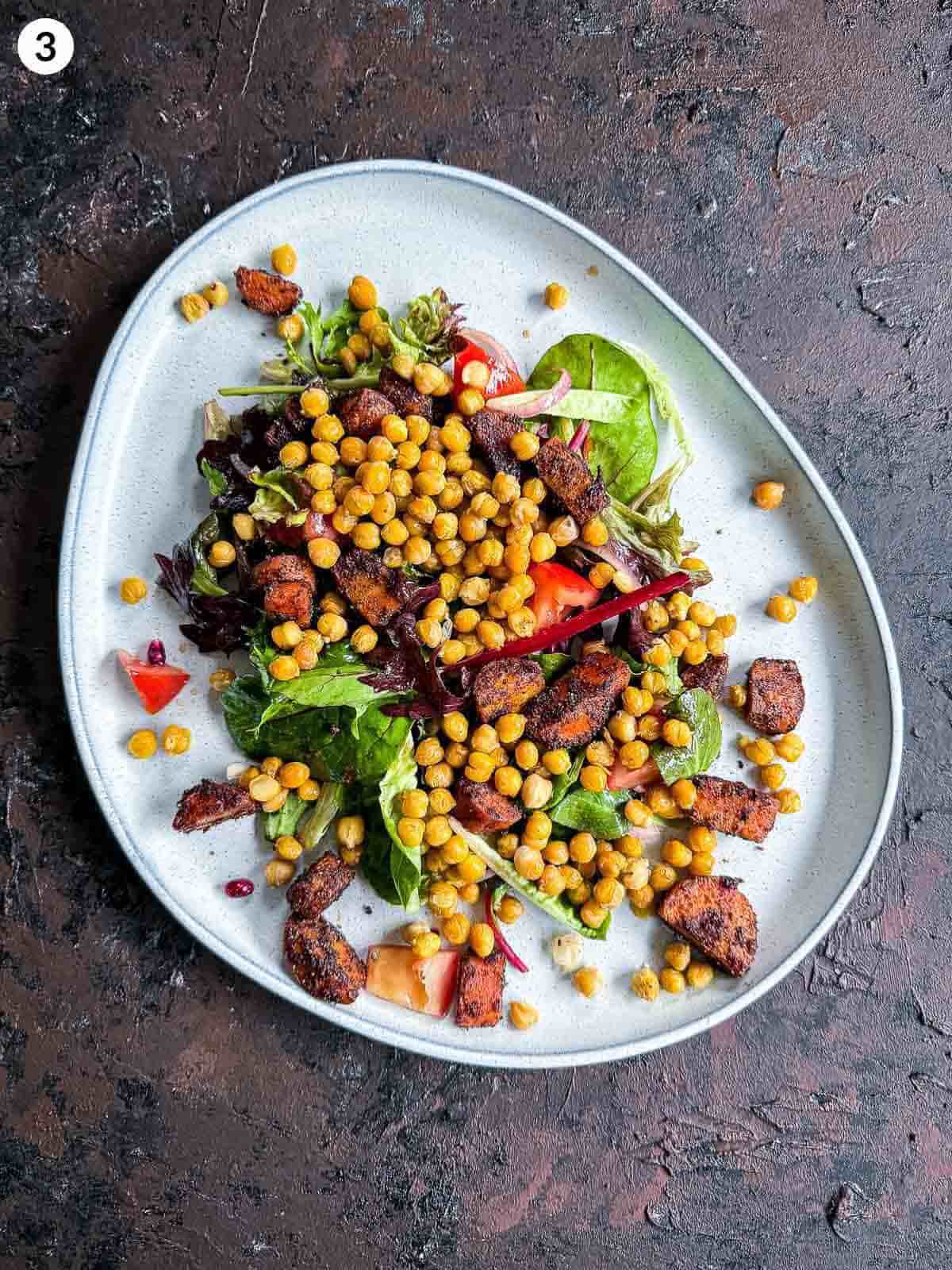Plating process shot for Roasted Chickpea and Carrot Baharat Salad on a grey platter against a dark background